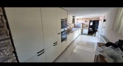 Dugačka kuhinja sa belim elementima i ugrađenim aparatima. - image 7