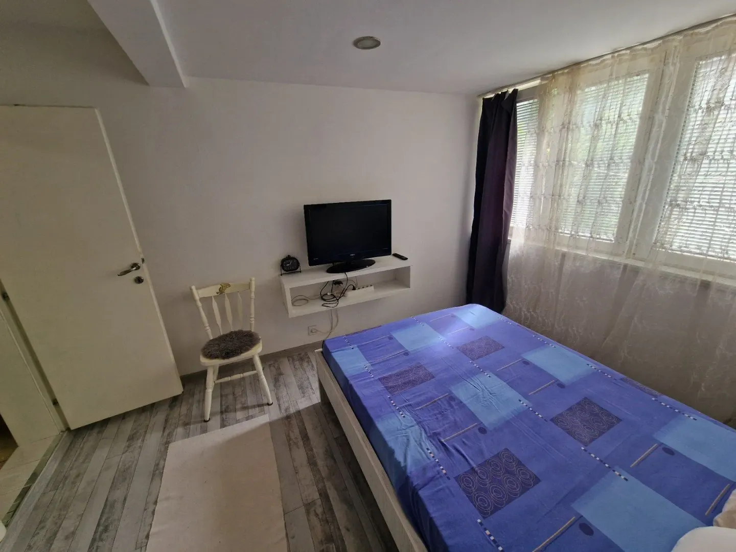 Bedroom with a bed, TV, and a white chair.
