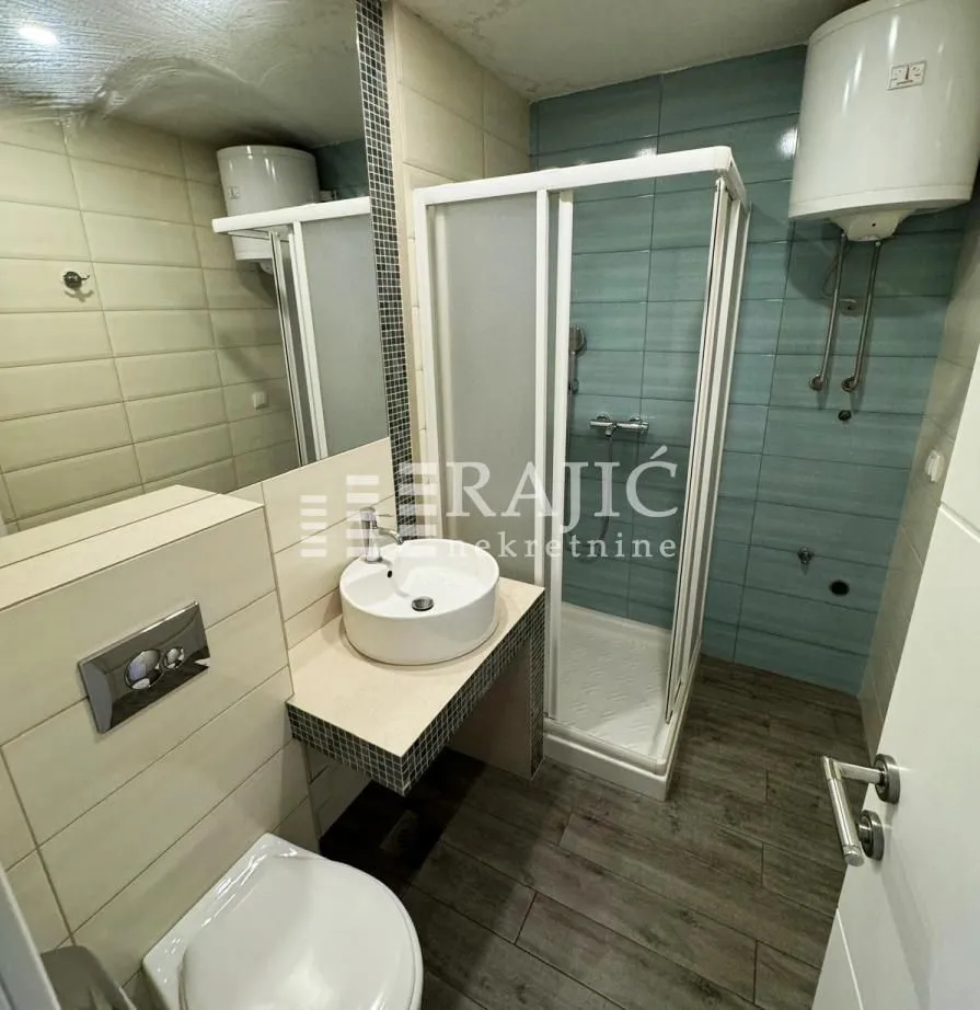 Smaller bathroom with a shower cabin, washbasin, and toilet.