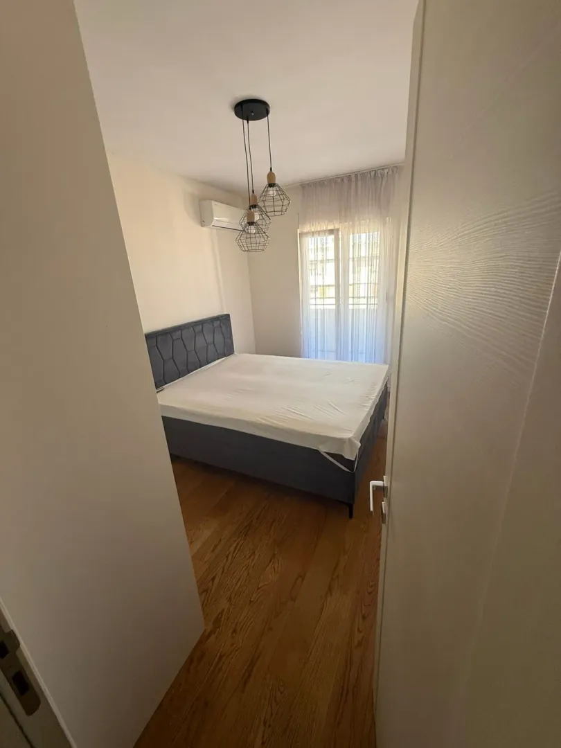 Bedroom with a double bed, wooden floor and a window with curtains.