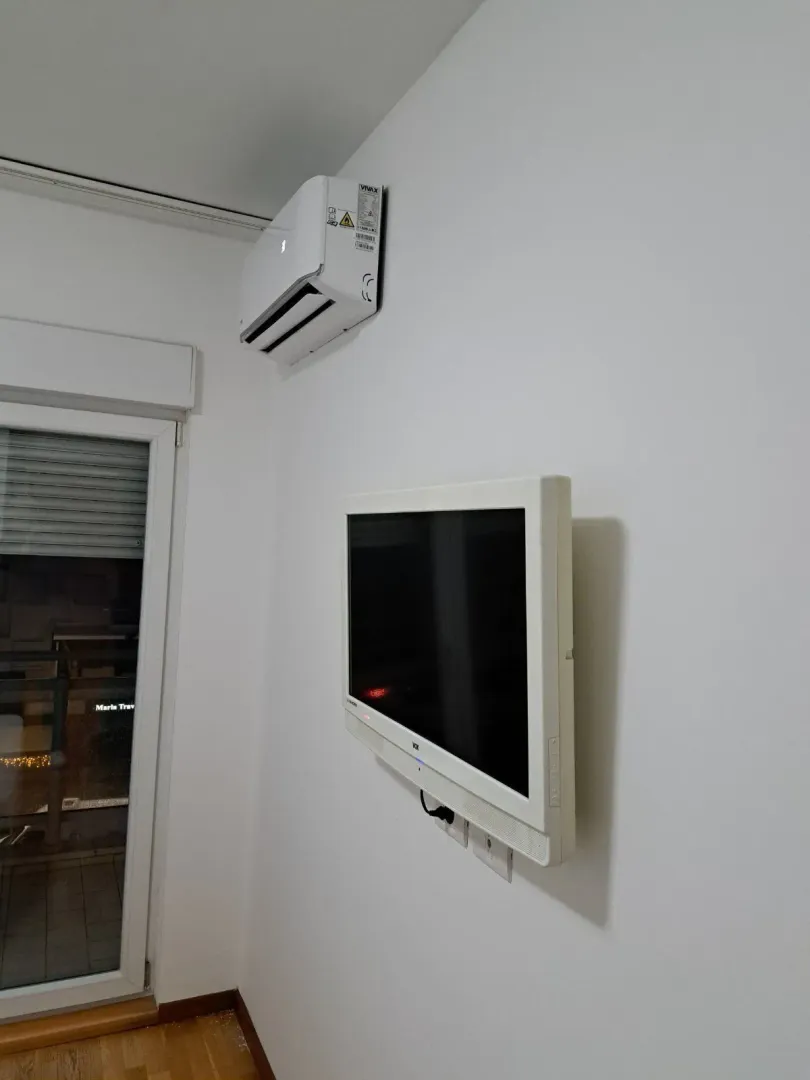 Bijeli zid sa montiranim televizorom i klima uređajem pored balkonskih vrata.