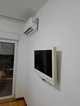 Bijeli zid sa montiranim televizorom i klima uređajem pored balkonskih vrata. - image 6