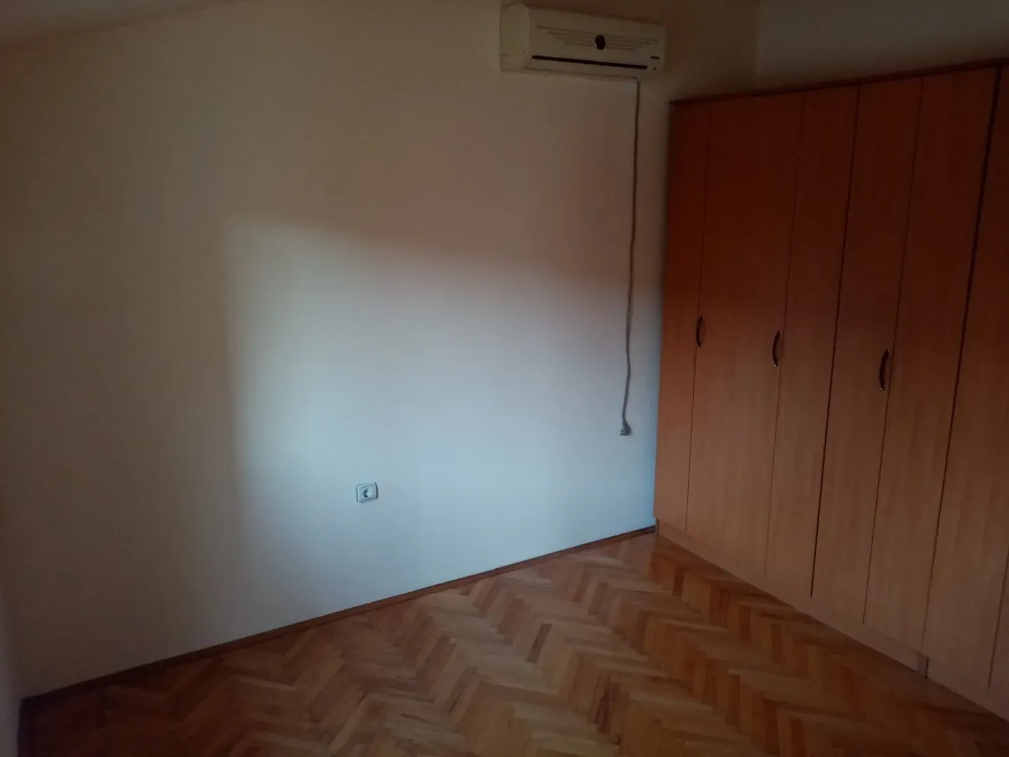 An empty room featuring a wooden wardrobe, air conditioning, and parquet flooring.