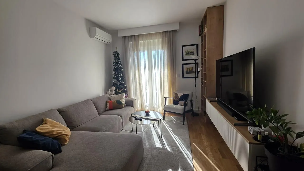 Dnevna soba sa ugaonom garniturom, televizorom i izlazom na terasu.