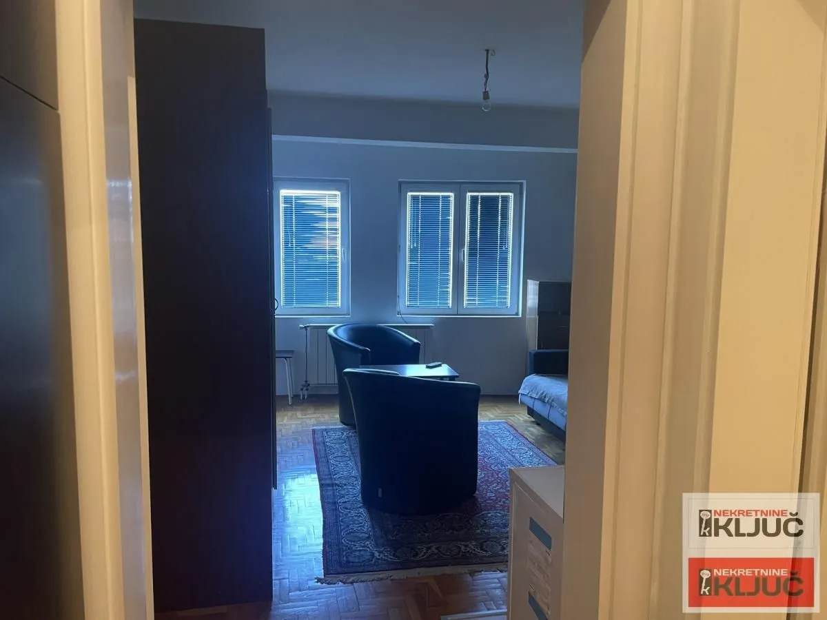 Pogled iz hodnika na dnevnu sobu sa foteljama i prozorima.