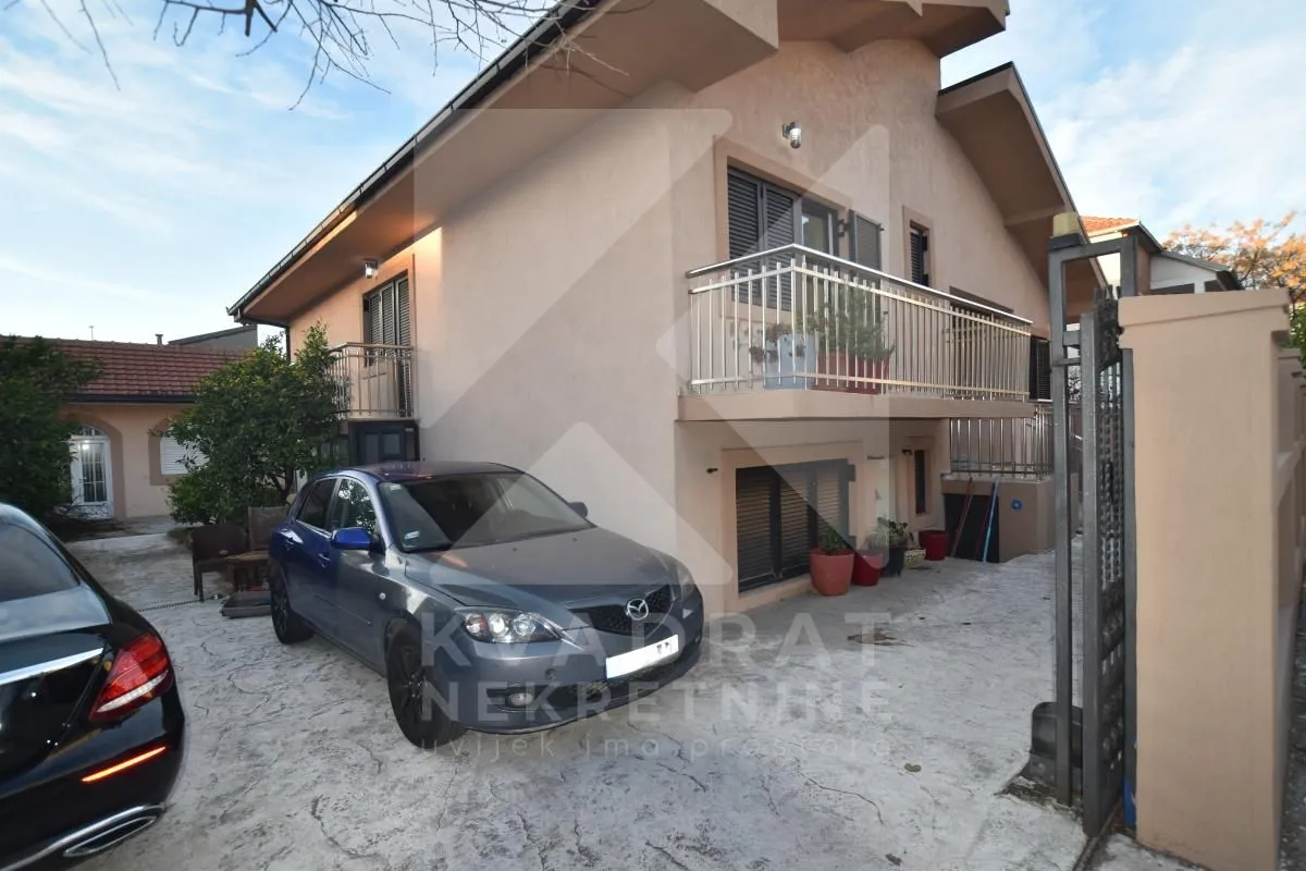 Exterior view of the house with a courtyard and parked cars.
