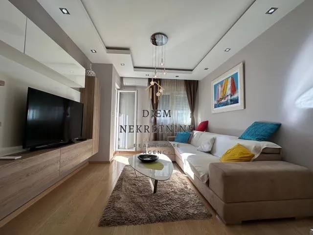 Living room with a sofa, TV, and drop ceiling with lighting.