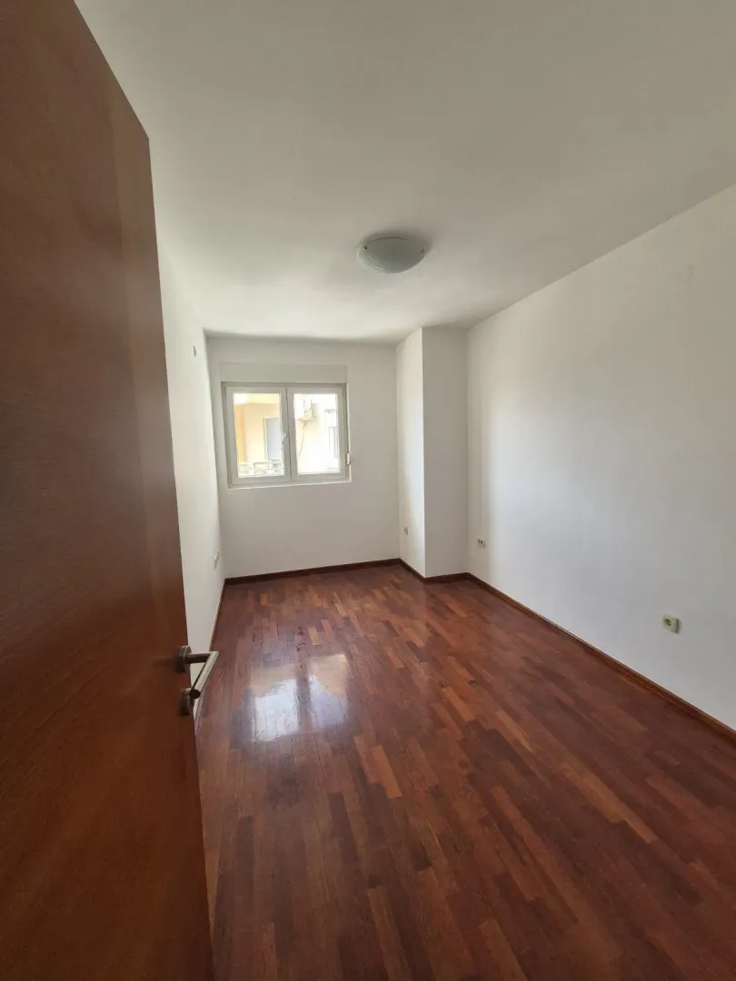 An empty room with parquet flooring and a single window.