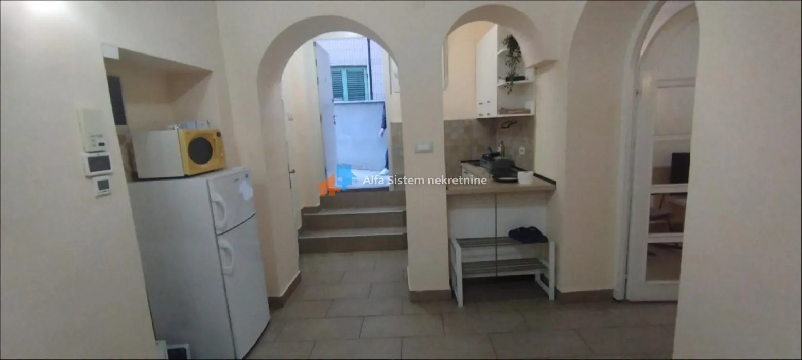 Smaller kitchen with a refrigerator and a passageway towards the exit.