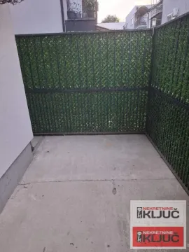 Manje popločano dvorište ograđeno metalnom ogradom sa veštačkom živom ogradom. - image 11