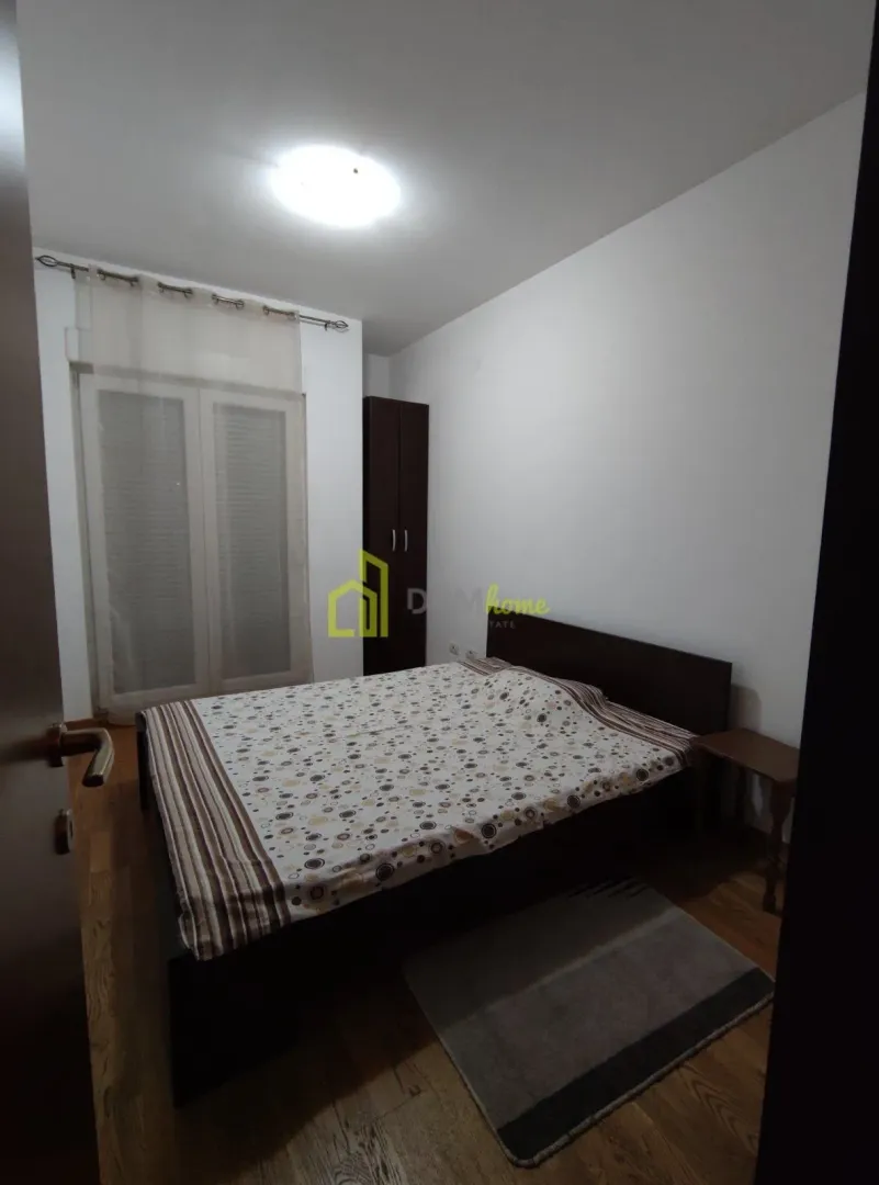 Namještena spavaća soba sa bračnim krevetom, ormarom i balkonskim vratima.