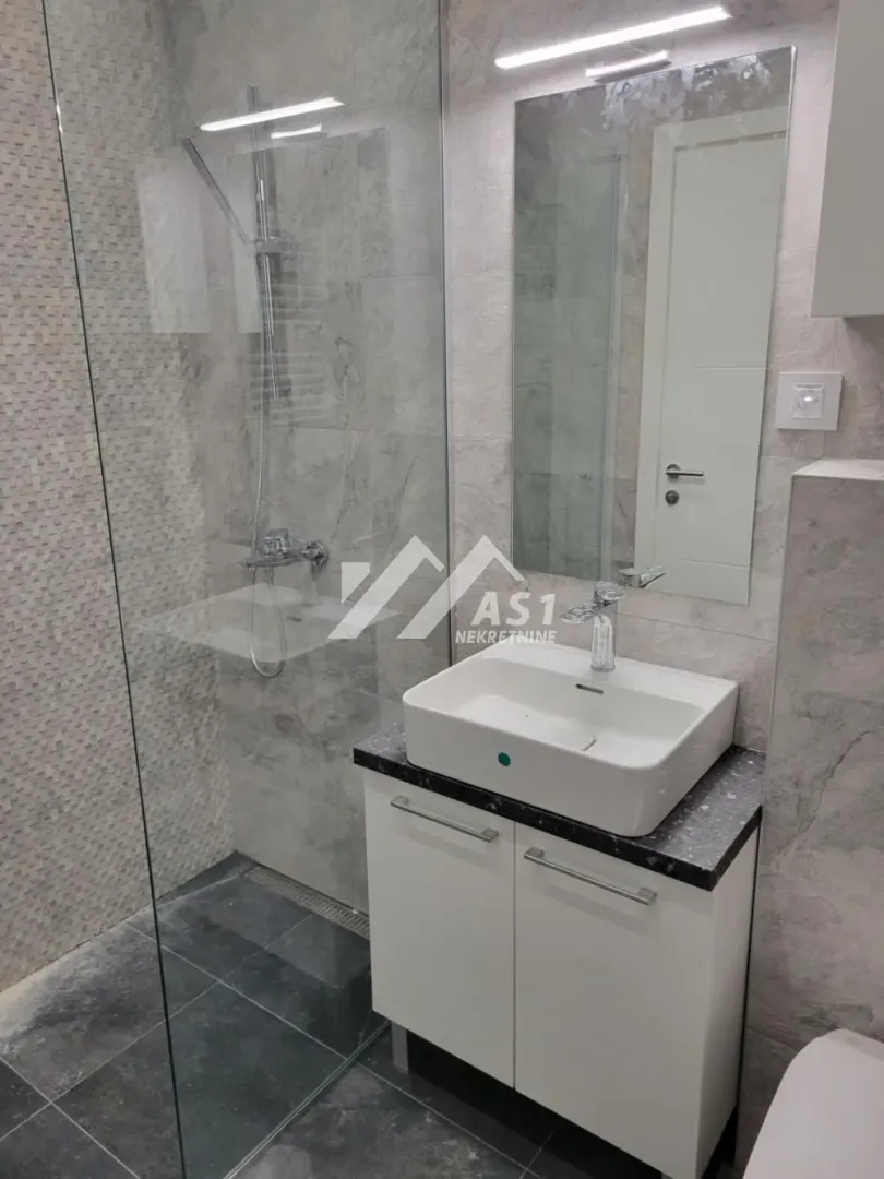 Moderno kupatilo sa tuš kabinom, umivaonikom i ogledalom.