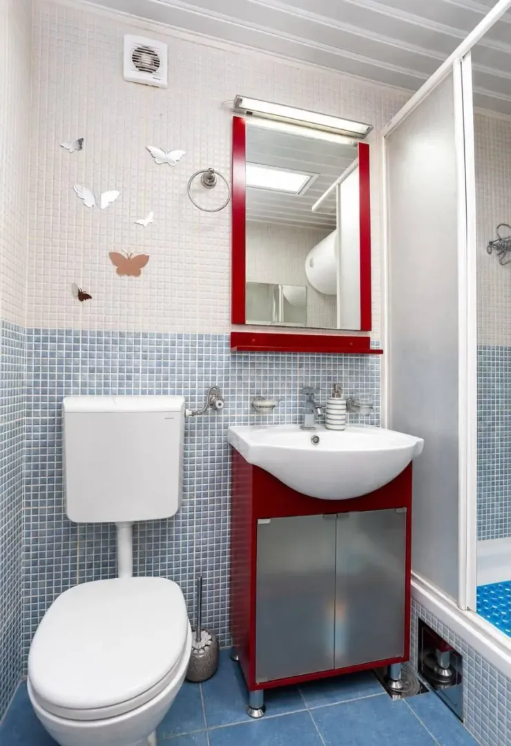 Small bathroom with mosaic tiles, a vanity with a red cabinet, and a shower enclosure.