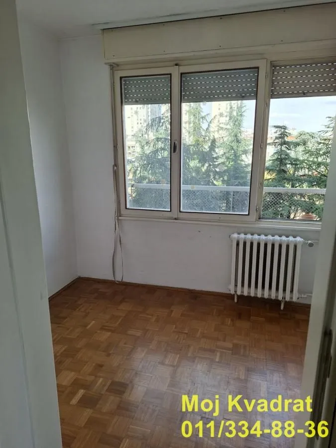 Prazna soba sa parketom i prozorom koji gleda na zelenilo.