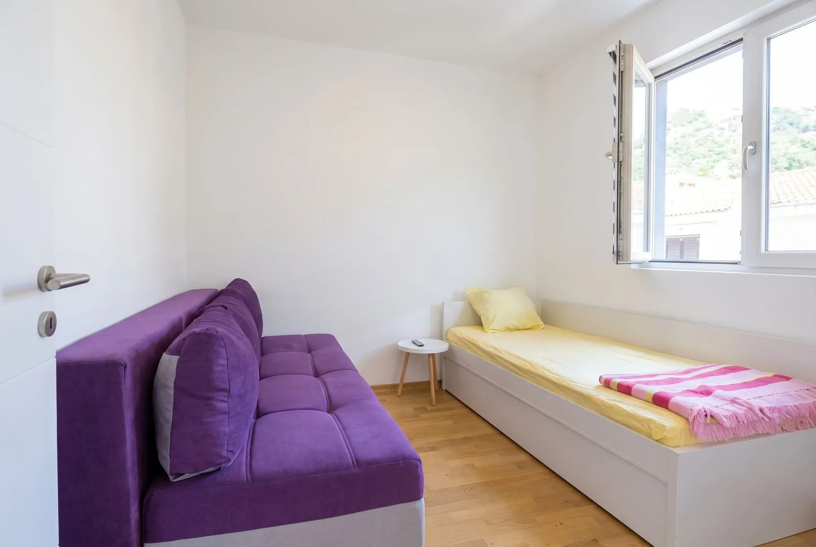 Small bedroom with a bed and a purple sofa next to the window.