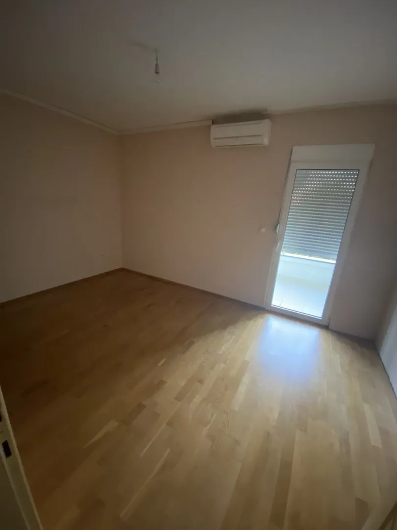 Prazna soba sa parketom, klima uređajem i izlazom na terasu.