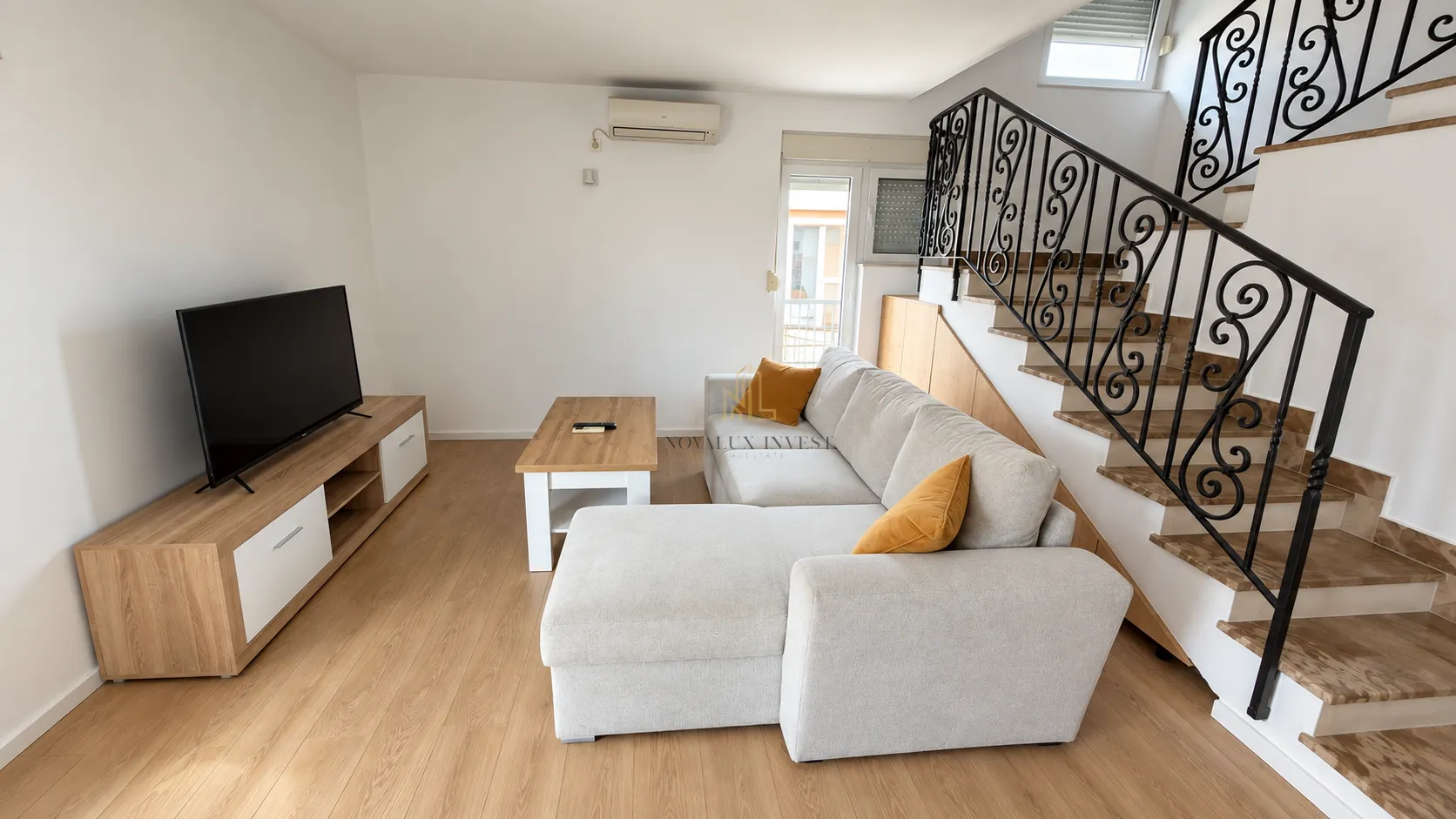 Living room with a corner sofa, TV unit, and staircase.