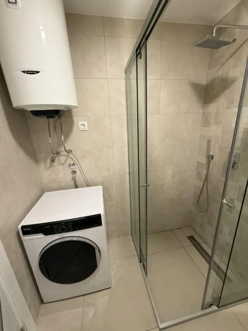Moderno opremljeno kupatilo sa tuš kabinom i veš mašinom.