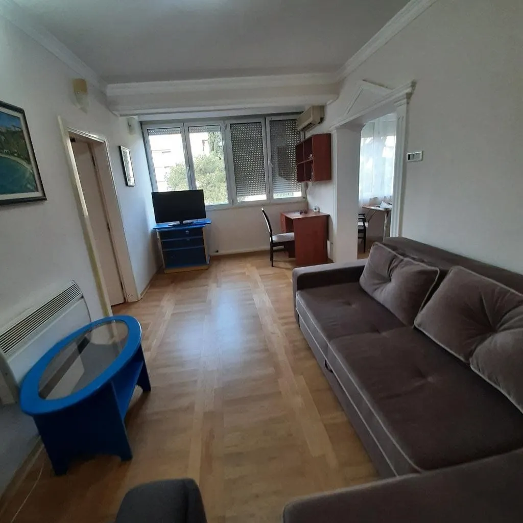 Dnevna soba sa garniturom za sedenje, TV-om i radnim stolom pored prozora.