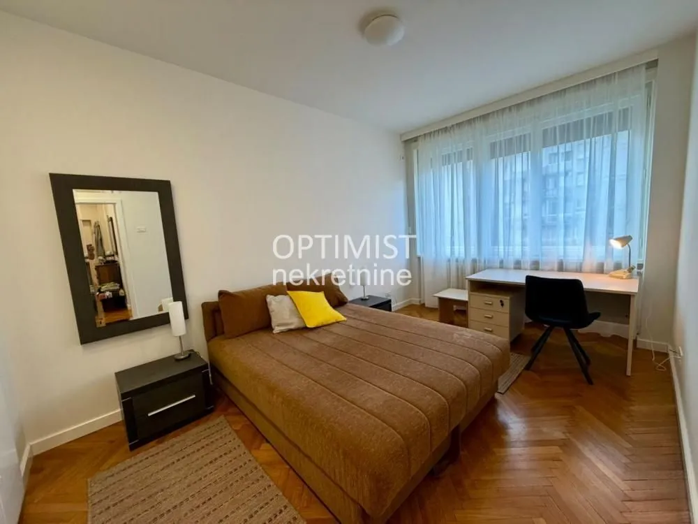 Furnished bedroom with a double bed, a desk, and parquet flooring.