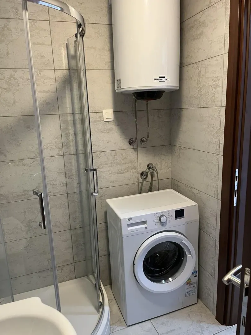 A modern bathroom with a shower cabin, washing machine, and water heater.