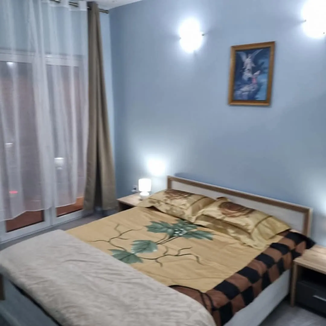 Namještena spavaća soba sa bračnim krevetom, noćnim stočićima i balkonskim vratima.