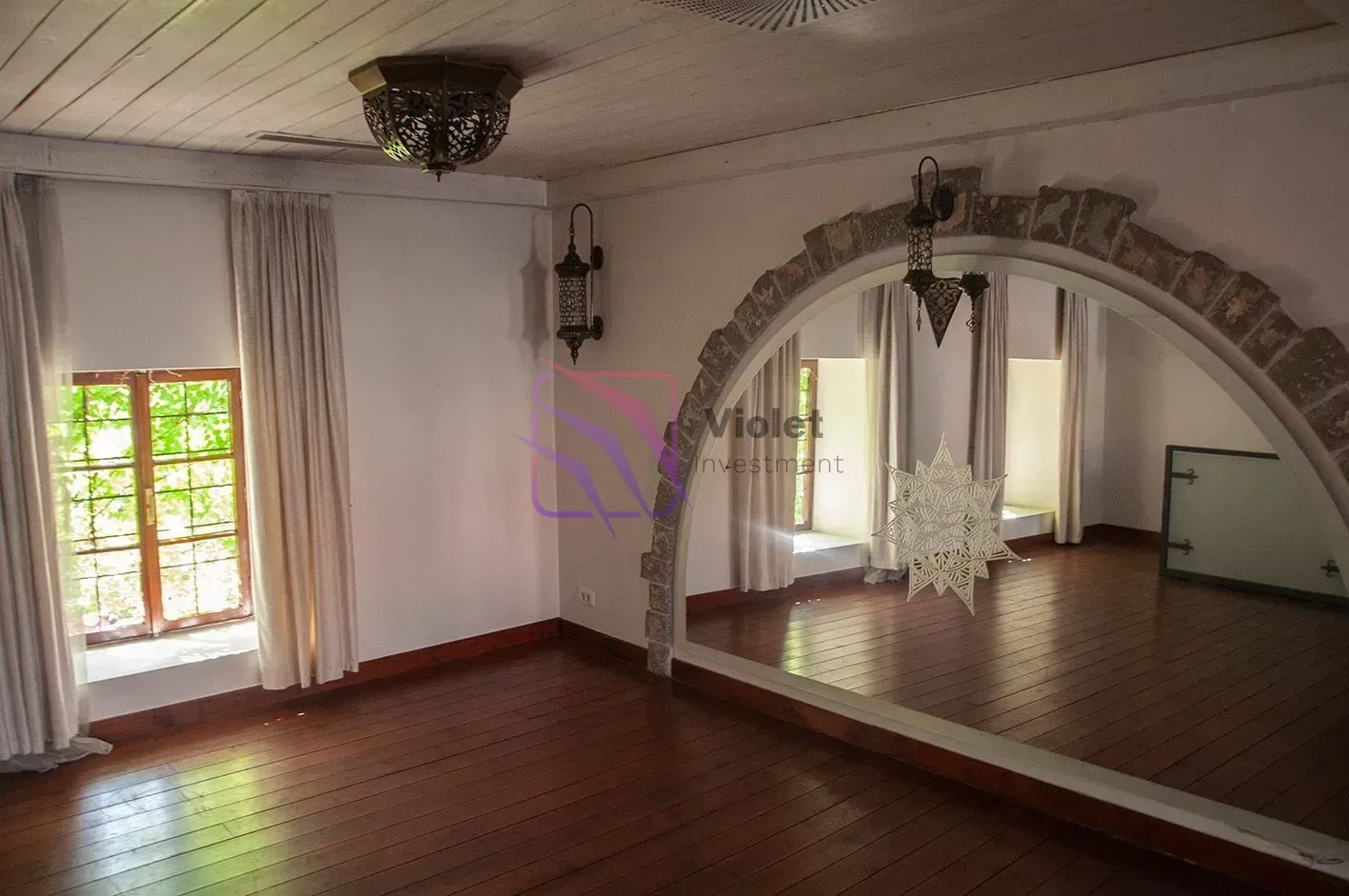 Spacious room with a wooden floor, plank ceiling, and a large mirror within a stone arch.