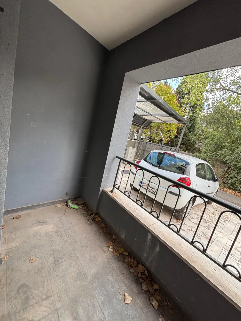 Natkriveni balkon sa pogledom na dvorište i parkirani automobil.