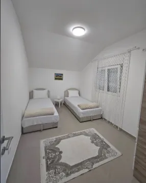 Svijetla spavaća soba sa dva kreveta za samce, tepihom i prozorom sa zavjesama. - image 10
