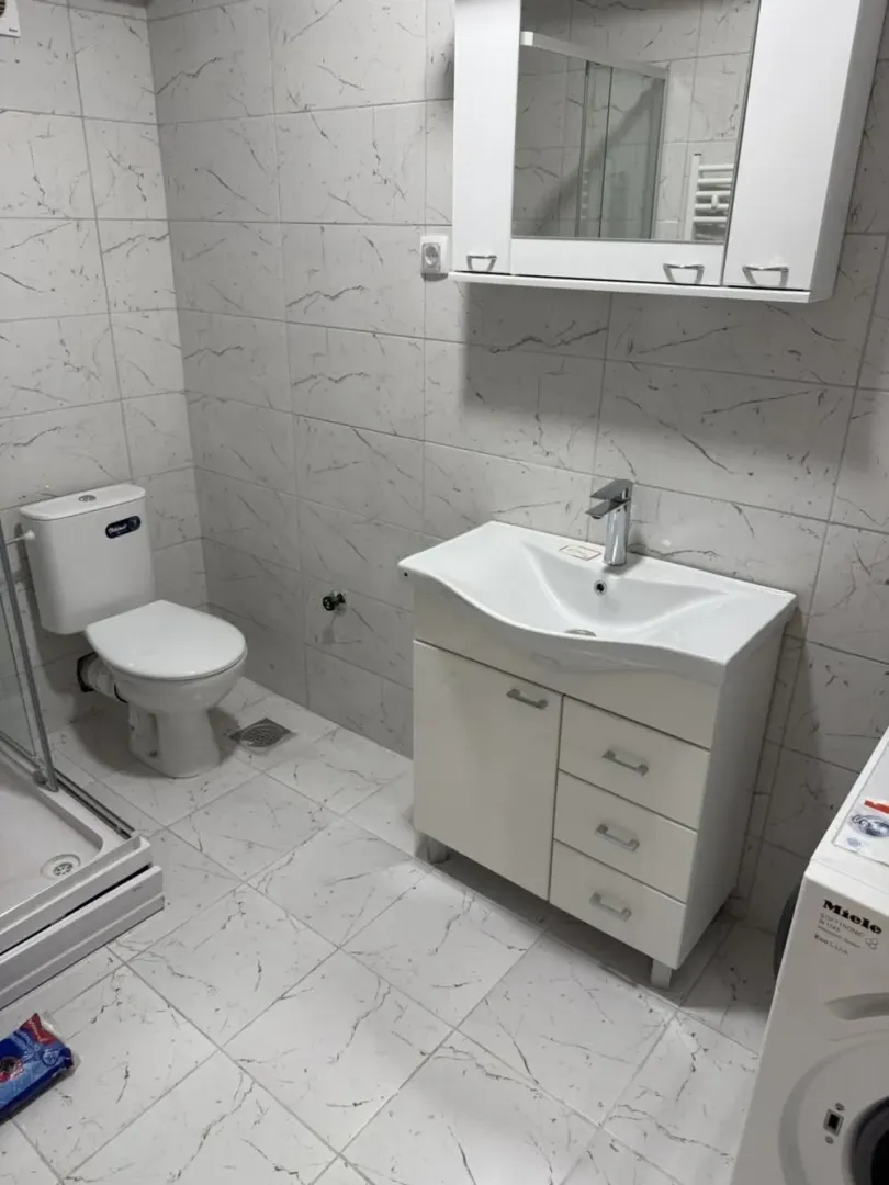 Potpuno opremljeno kupatilo sa belim keramičkim pločicama, umivaonikom i wc šoljom.