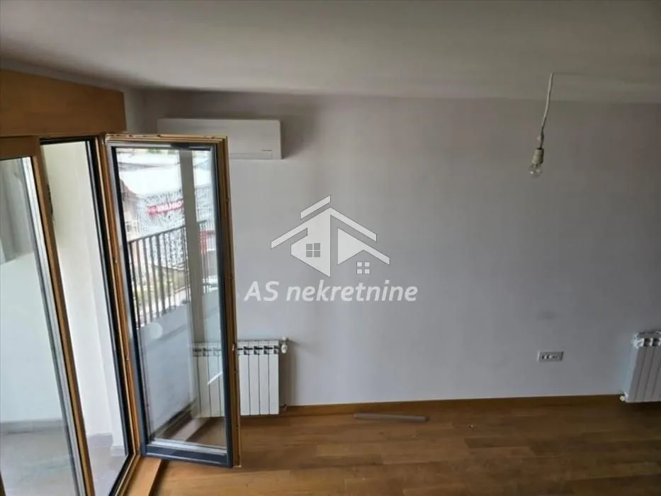 Empty room with wooden flooring, radiator, and balcony access.