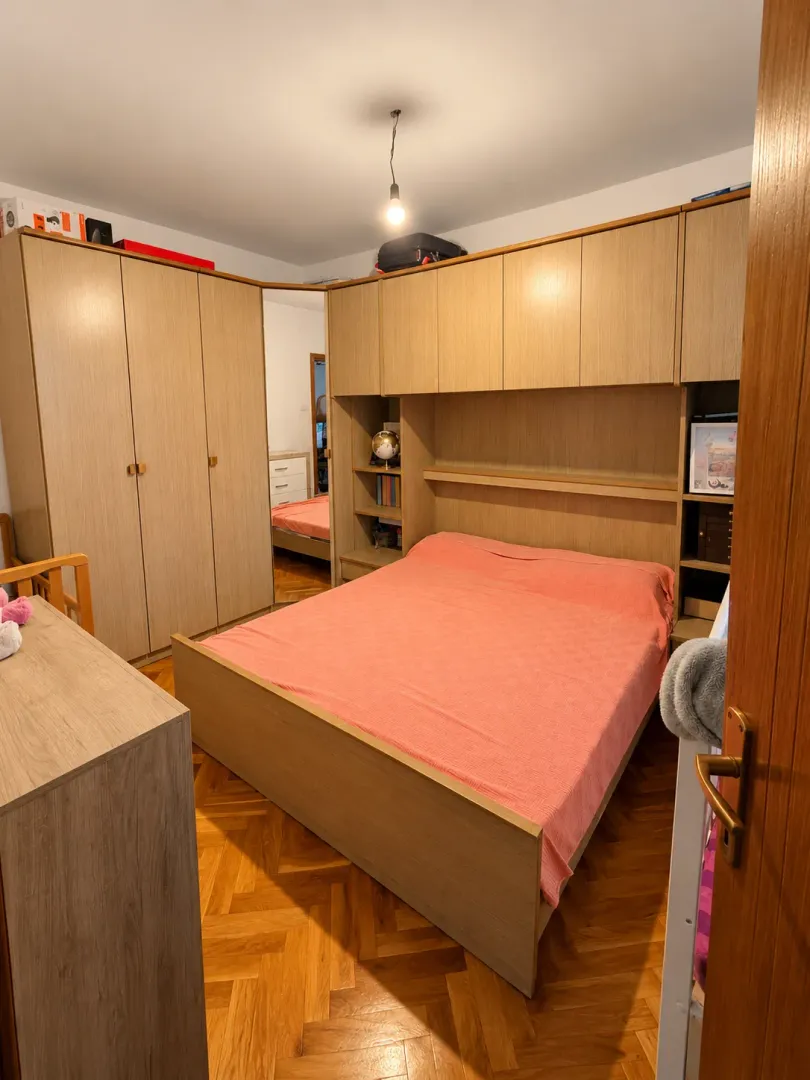 Namještena spavaća soba sa bračnim krevetom, drvenim garderoberom i parketom na podu.