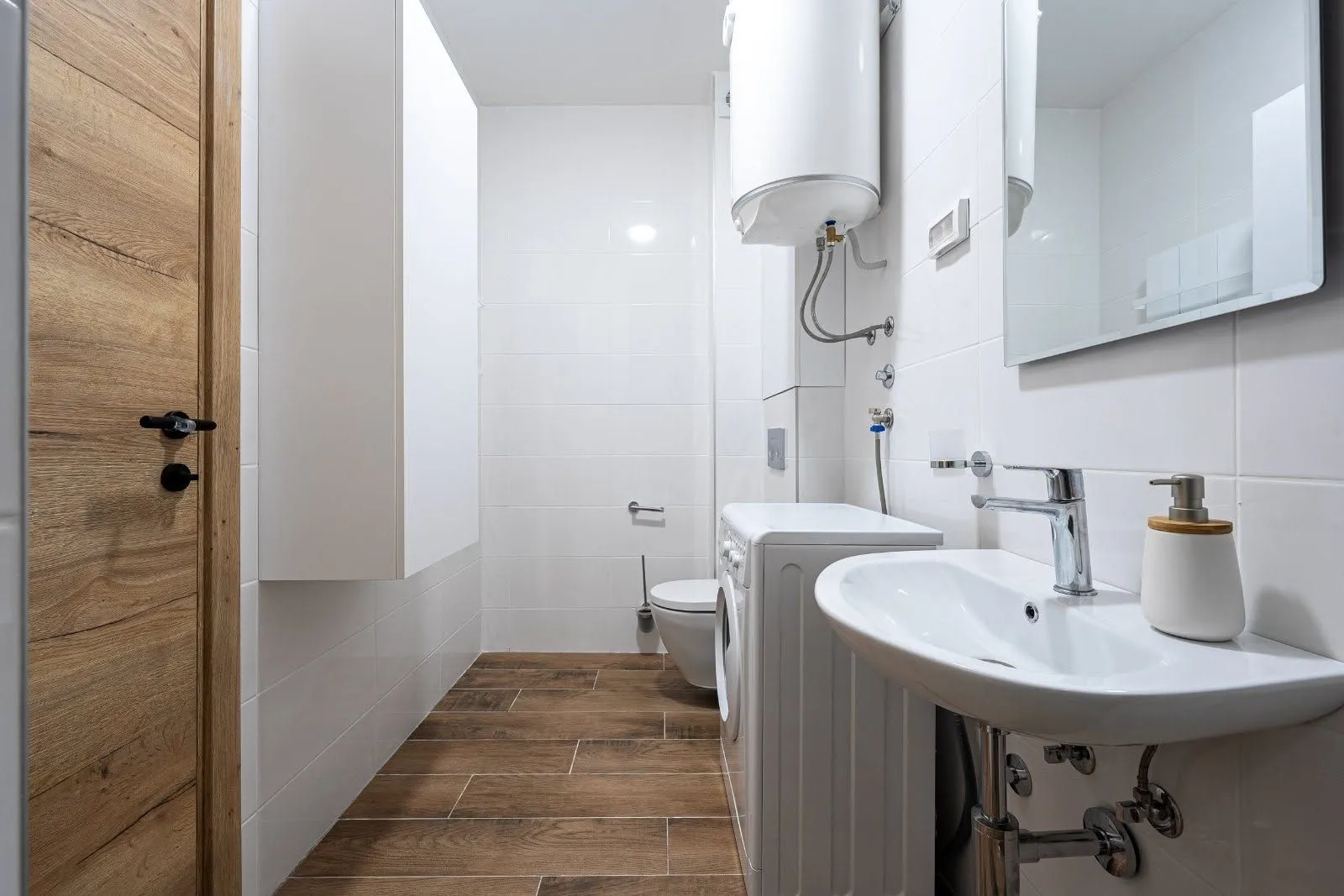 Moderne kupatilo sa bijelim pločicama, umivaonikom, veš mašinom i WC šoljom.