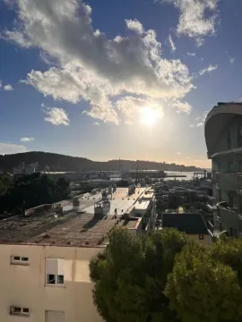 Pogled sa prozora na okolne zgrade i luku sa brdima u pozadini. - image 3