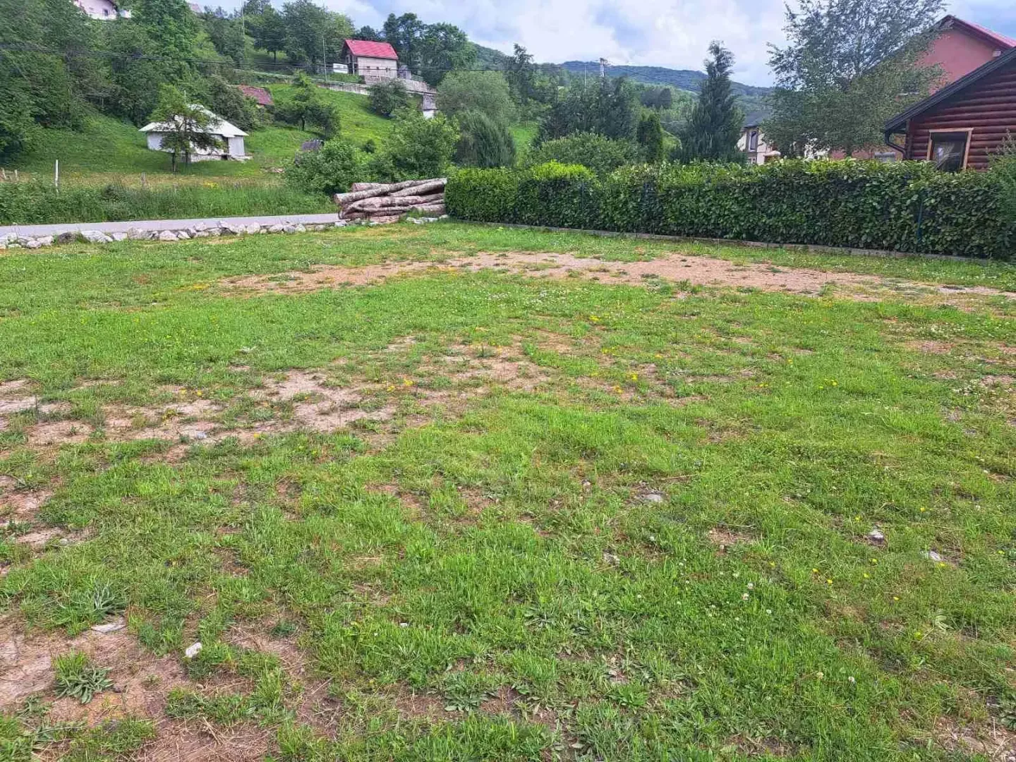 Prostrani travnati plac okružen zelenilom.