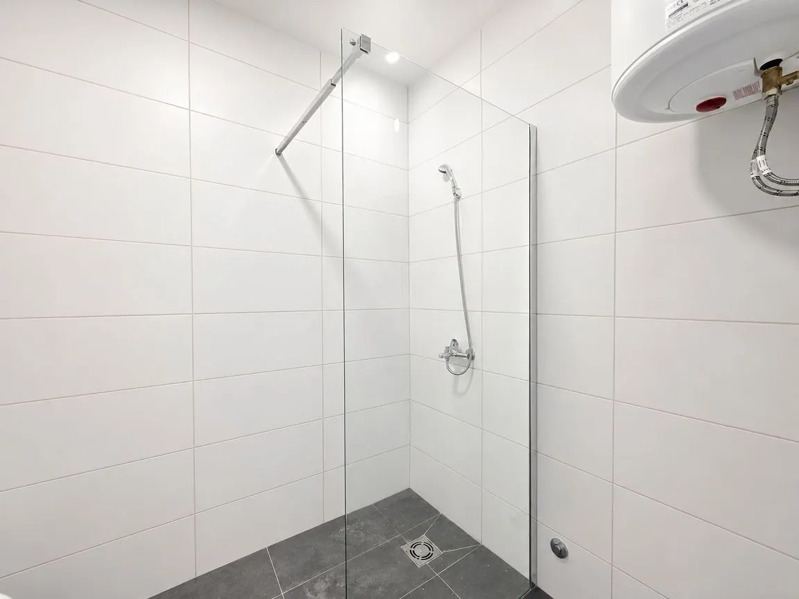 Moderne kupatilo sa tuš kabinom od stakla i bijelim pločicama.