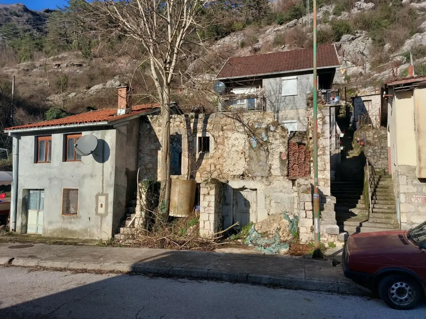 Pogled na starije kuće i dvorište u brdskom okruženju.