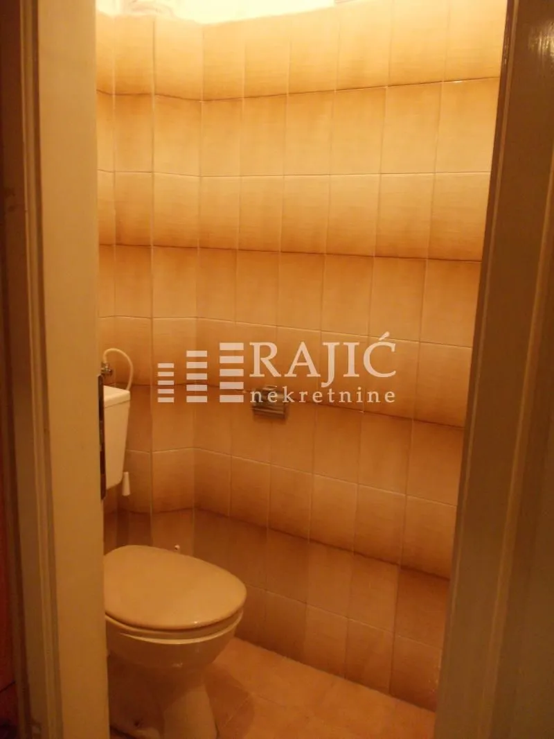 Small bathroom lined with beige ceramic tiles containing a toilet.