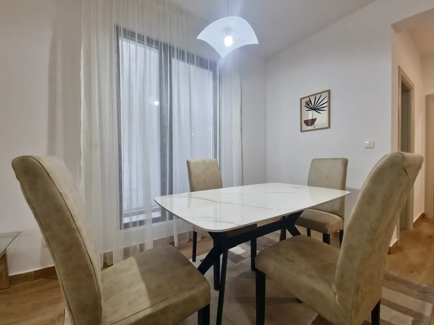 Dining area with a table and four chairs next to a window with white curtains.