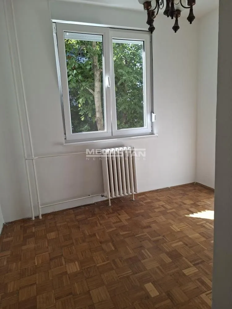 Prazna soba sa parketom i prozorom koji gleda na zelenilo.
