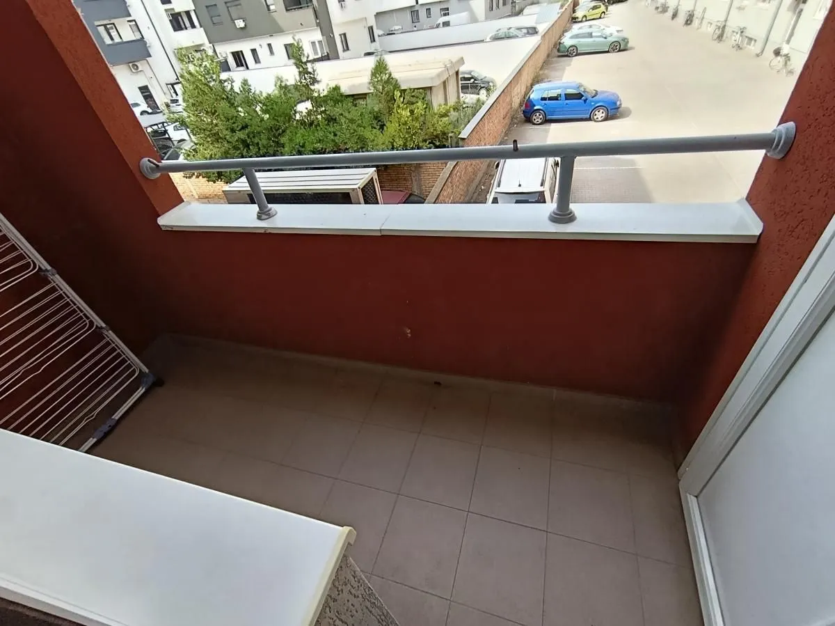 Manji popločani balkon sa metalnom ogradom i pogledom na parking i okolne zgrade.