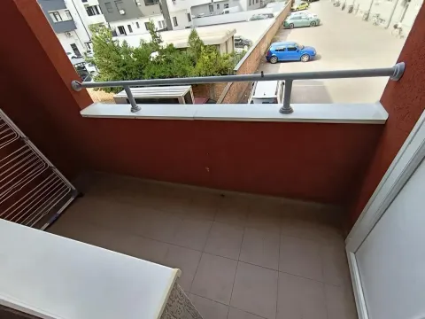 Manji popločani balkon sa metalnom ogradom i pogledom na parking i okolne zgrade. - image 21