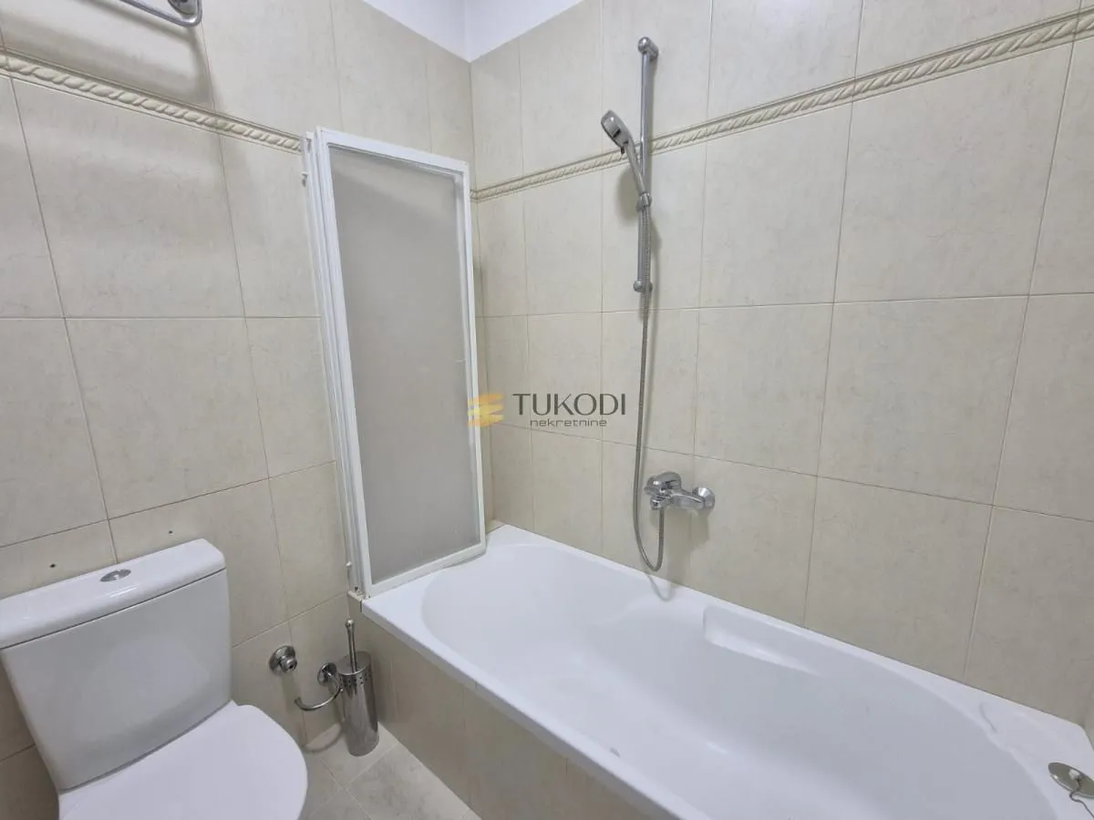 Kupatilo opremljeno kadom, tušem i sanitarijama obloženo svetlim pločicama.