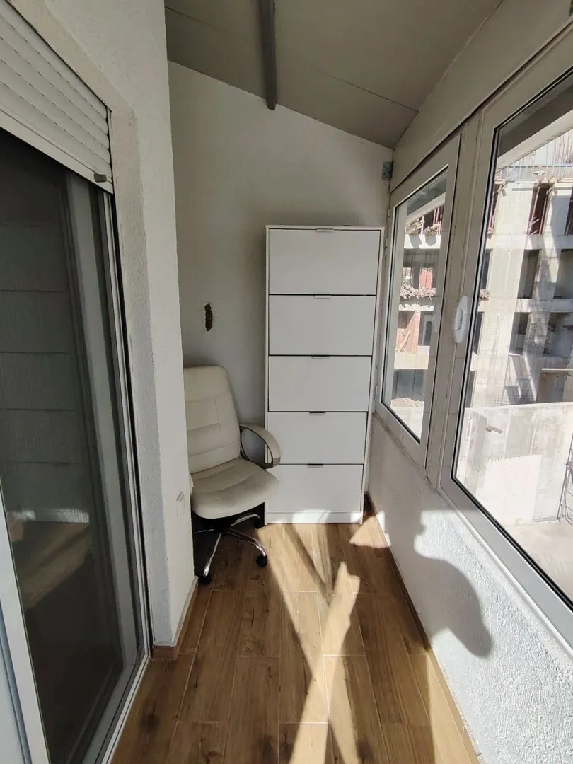 Zastakljeni balkon sa bijelom komodom i kancelarijskom stolicom.