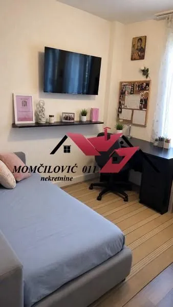 Dnevna soba sa krevetom, radnim stolom i televizorom na zidu.