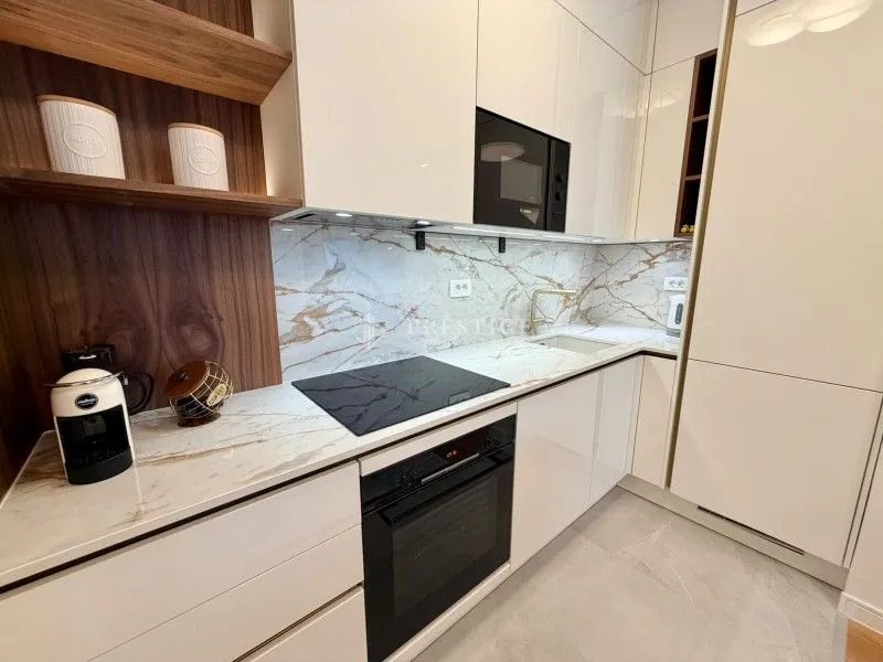 Moderna kuhinja sa bijelim elementima, drvenim detaljima i ugradnom tehnikom.
