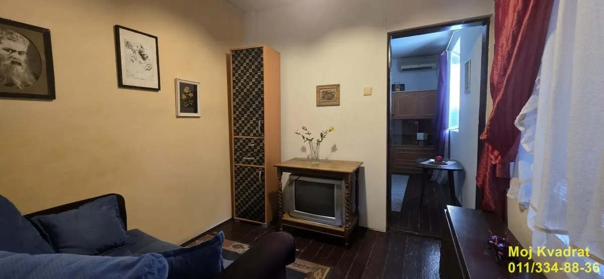 Manja dnevna soba sa garniturom, televizorom i slikama na zidu.