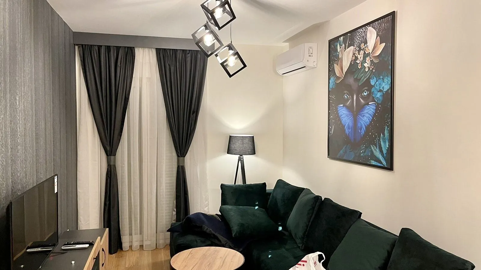 Dnevna soba sa tamnozelenom ugaonom garniturom, dekorativnom slikom i modernim osvjetljenjem.