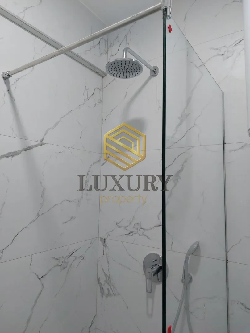Modern walk-in shower with marble-look tiles and overhead shower head.