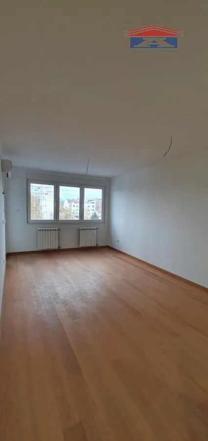 Empty room with wooden flooring and windows.